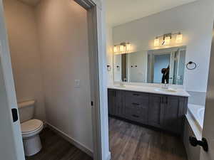 Bathroom featuring a bath, double vanity, hardwood / wood-style flooring, and toilet