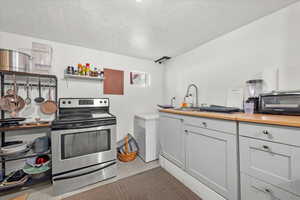 Kitchen with stainless steel electric stove, wood counters, sink, and a textured ceiling