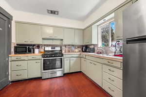 Kitchen with tasteful backsplash, dark hardwood / wood-style flooring, appliances with stainless steel finishes, and green cabinets