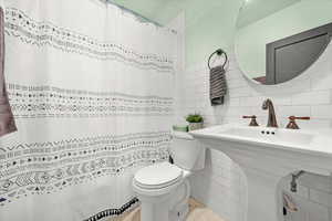 Bathroom with toilet, tile patterned floors, decorative backsplash, and tile walls