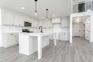 Kitchen featuring light wood finished floors, decorative backsplash, light countertops, appliances with stainless steel finishes, and pendant lighting
