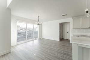 Unfurnished dining area featuring visible vents, light wood-style flooring, baseboards, and an inviting chandelier