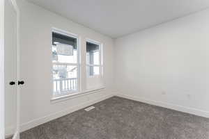 Empty room featuring visible vents, baseboards, and dark colored carpet
