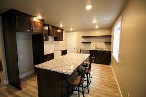 Kitchen with a kitchen bar, light hardwood / wood-style flooring, sink, light stone counters, and a kitchen island