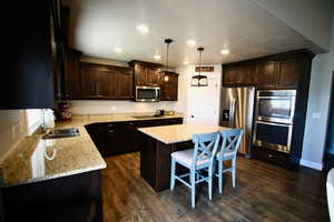 Kitchen featuring stainless steel appliances, sink, hanging light fixtures, a kitchen island, and dark hardwood / wood-style flooring