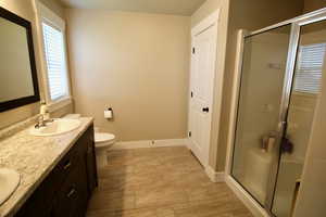 Bathroom with toilet, double sink vanity, tile patterned flooring, and an enclosed shower