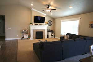 Living room featuring a fireplace, carpet flooring, vaulted ceiling, and ceiling fan