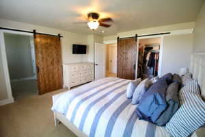 Carpeted bedroom with ceiling fan, a closet, a barn door, and a spacious closet