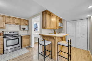 Kitchen featuring light hardwood / wood-style floors, sink, stainless steel electric range oven, and a kitchen bar