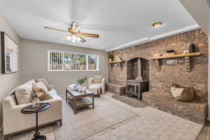 Living room with a wood stove, carpet, brick wall, and ceiling fan