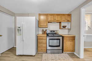 Kitchen with stainless steel electric range, white refrigerator with ice dispenser, and light wood-type flooring