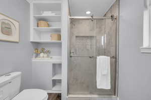 Bathroom with wood-type flooring, a shower with shower door, and toilet