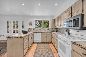 Kitchen featuring kitchen peninsula, light tile patterned flooring, decorative backsplash, and white appliances