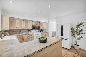 Kitchen featuring white appliances, sink, light brown cabinets, backsplash, and light tile patterned floors