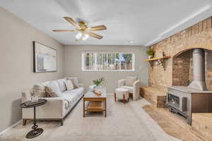 Living room with brick wall, light carpet, a wood stove, and ceiling fan