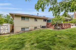 Back of property featuring a deck, central AC unit, a lawn, and a shed