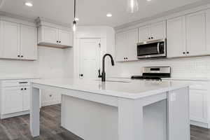 Kitchen featuring dark hardwood / wood-style flooring, stainless steel appliances, sink, pendant lighting, and an island with sink