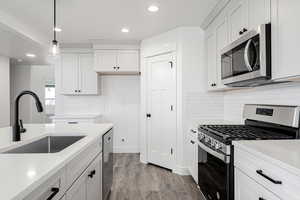 Kitchen with white cabinetry, sink, light hardwood / wood-style floors, decorative light fixtures, and appliances with stainless steel finishes