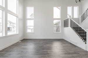 Unfurnished living room with a towering ceiling, an inviting chandelier, and dark wood-type flooring