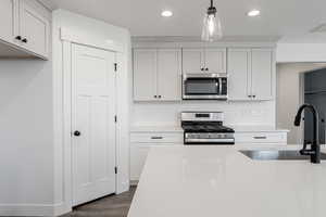 Kitchen with white cabinetry, sink, stainless steel appliances, dark hardwood / wood-style floors, and decorative light fixtures