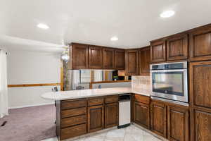 Kitchen featuring dark brown cabinets, stainless steel oven, kitchen peninsula, ceiling fan, and light carpet