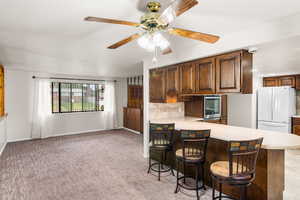 Kitchen featuring white fridge, ceiling fan, light carpet, kitchen peninsula, and backsplash