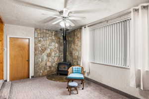 Unfurnished room featuring a textured ceiling, ceiling fan, and a wood stove