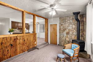 Sitting room featuring a wood stove, carpet floors, a textured ceiling, and ceiling fan