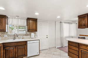 Kitchen featuring sink, light tile patterned flooring, white dishwasher, and tasteful backsplash