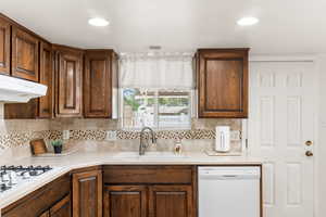 Kitchen with decorative backsplash, white appliances, and sink