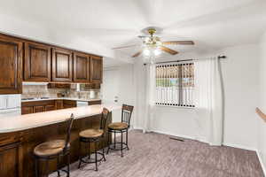 Kitchen featuring white dishwasher, a breakfast bar, kitchen peninsula, decorative backsplash, and ceiling fan