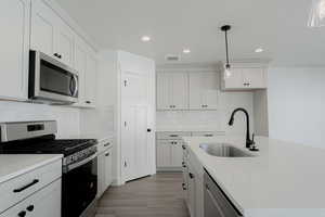 Kitchen featuring sink, appliances with stainless steel finishes, decorative light fixtures, light hardwood / wood-style floors, and white cabinetry