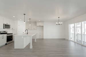 Kitchen featuring light hardwood / wood-style flooring, a notable chandelier, an island with sink, pendant lighting, and appliances with stainless steel finishes