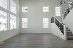 Unfurnished living room featuring dark hardwood / wood-style flooring, a towering ceiling, and a chandelier