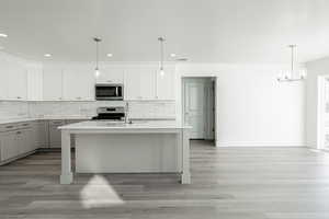 Kitchen with a kitchen island with sink, white cabinets, sink, decorative light fixtures, and stainless steel appliances