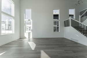 Unfurnished living room featuring a notable chandelier, a healthy amount of sunlight, wood-type flooring, and a towering ceiling