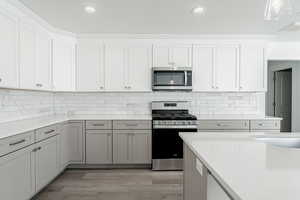 Kitchen with hanging light fixtures, decorative backsplash, light stone countertops, appliances with stainless steel finishes, and light hardwood / wood-style floors