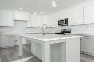 Kitchen with pendant lighting, light hardwood / wood-style floors, stainless steel appliances, and an island with sink