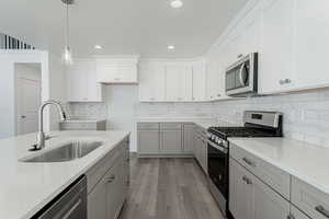 Kitchen featuring light stone counters, stainless steel appliances, sink, pendant lighting, and light hardwood / wood-style flooring