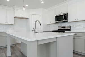 Kitchen featuring stainless steel appliances, a kitchen island with sink, pendant lighting, light hardwood / wood-style flooring, and white cabinetry