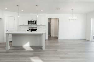 Kitchen featuring stainless steel appliances, decorative light fixtures, a center island with sink, a chandelier, and white cabinetry