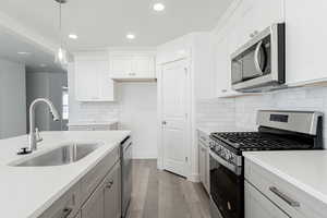 Kitchen featuring sink, stainless steel appliances, light hardwood / wood-style flooring, pendant lighting, and white cabinets