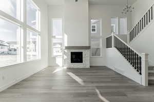 Unfurnished living room with hardwood / wood-style floors, a notable chandelier, a towering ceiling, and a fireplace