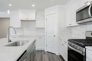 Kitchen with white cabinets, appliances with stainless steel finishes, hardwood / wood-style floors, and sink