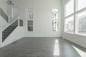 Unfurnished living room with a towering ceiling, dark hardwood / wood-style flooring, and an inviting chandelier