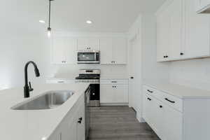 Kitchen with white cabinetry, sink, hanging light fixtures, dark hardwood / wood-style floors, and appliances with stainless steel finishes