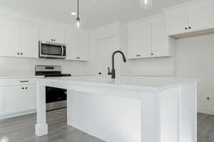 Kitchen with stainless steel appliances, pendant lighting, a center island with sink, light hardwood / wood-style flooring, and white cabinetry