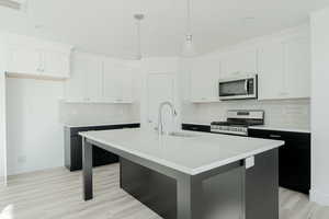 Kitchen with a kitchen island with sink, stove, white cabinets, and sink