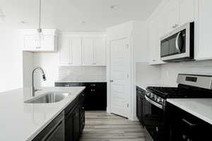 Kitchen with white cabinets, decorative light fixtures, sink, and stainless steel appliances