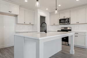 Kitchen with a kitchen island with sink, hanging light fixtures, white cabinets, and stainless steel appliances